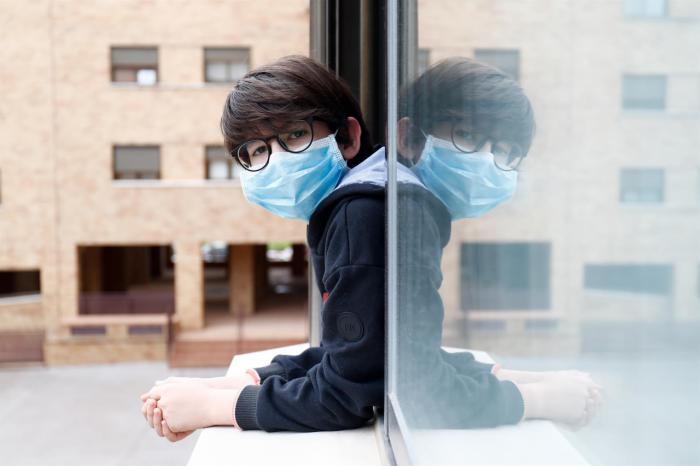 Un niño con una mascarilla se asoma a la ventana de su casa durante el confinamiento por el coronavirus